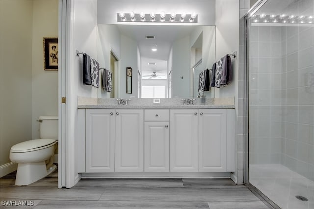 bathroom with toilet, a shower with shower door, double sink vanity, ceiling fan, and hardwood / wood-style flooring