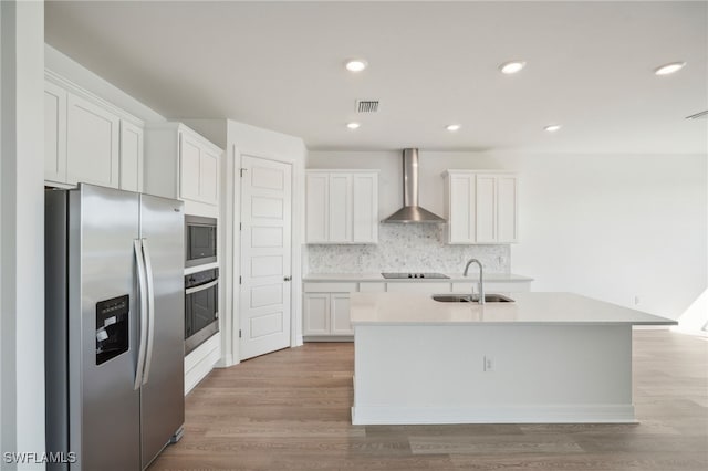 kitchen with a kitchen island with sink, sink, white cabinets, wall chimney exhaust hood, and appliances with stainless steel finishes