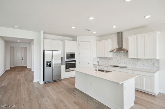 kitchen with sink, white cabinetry, wall chimney range hood, light hardwood / wood-style flooring, and appliances with stainless steel finishes