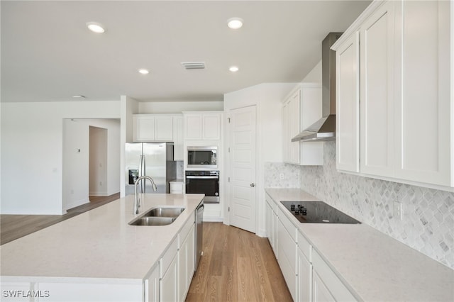 kitchen featuring light hardwood / wood-style floors, a kitchen island with sink, sink, wall chimney range hood, and appliances with stainless steel finishes