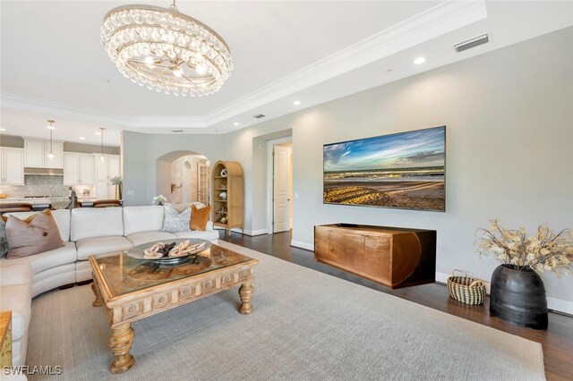 living room with dark hardwood / wood-style floors, crown molding, a tray ceiling, and a chandelier