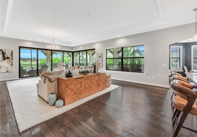 living room featuring baseboards, an inviting chandelier, recessed lighting, hardwood / wood-style floors, and a raised ceiling