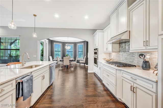 kitchen featuring arched walkways, dark wood finished floors, appliances with stainless steel finishes, under cabinet range hood, and a sink