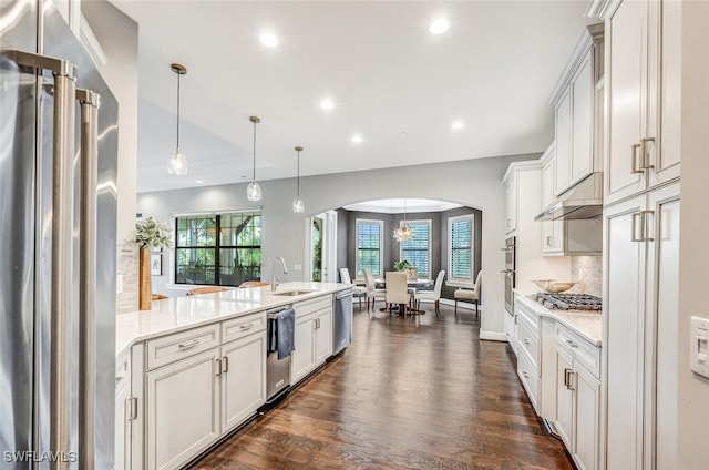 kitchen with light stone countertops, sink, hanging light fixtures, stainless steel appliances, and tasteful backsplash