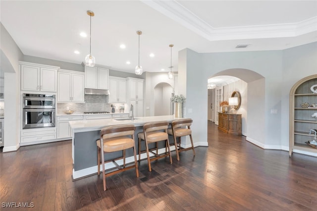 kitchen featuring double oven, a raised ceiling, white cabinetry, and hanging light fixtures