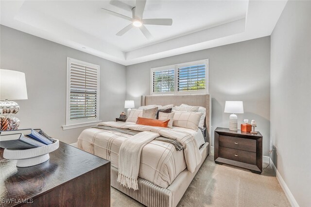 carpeted bedroom with ceiling fan, a raised ceiling, and multiple windows