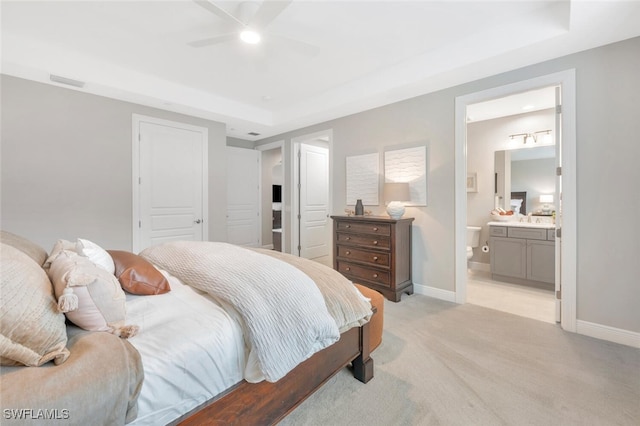 bedroom with a tray ceiling, light colored carpet, baseboards, and ensuite bath