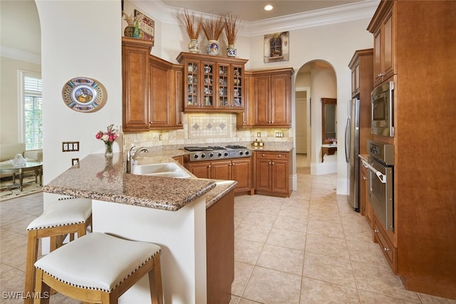 kitchen featuring a kitchen bar, sink, decorative backsplash, stainless steel appliances, and kitchen peninsula