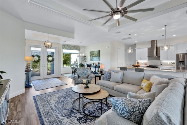 living room with ceiling fan with notable chandelier, a raised ceiling, french doors, and light hardwood / wood-style floors