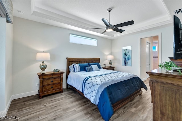 bedroom featuring a tray ceiling, visible vents, baseboards, and wood finished floors