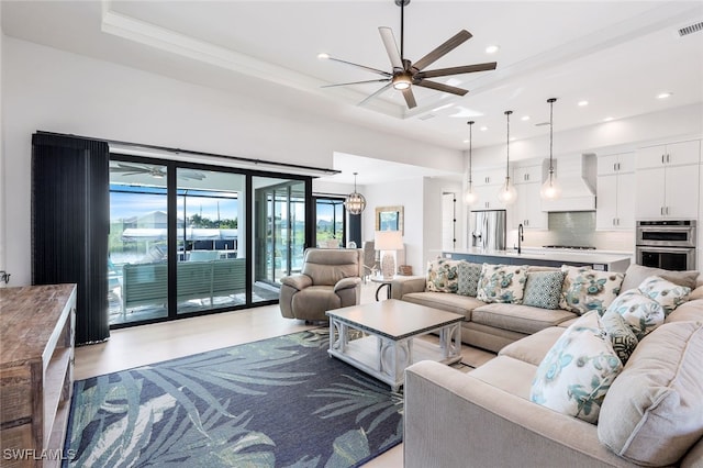 living room with ceiling fan, a raised ceiling, and sink