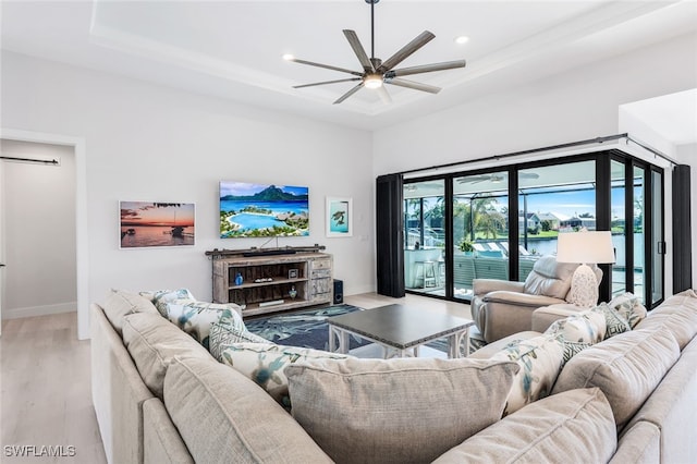 living room featuring light wood-type flooring, a raised ceiling, and ceiling fan