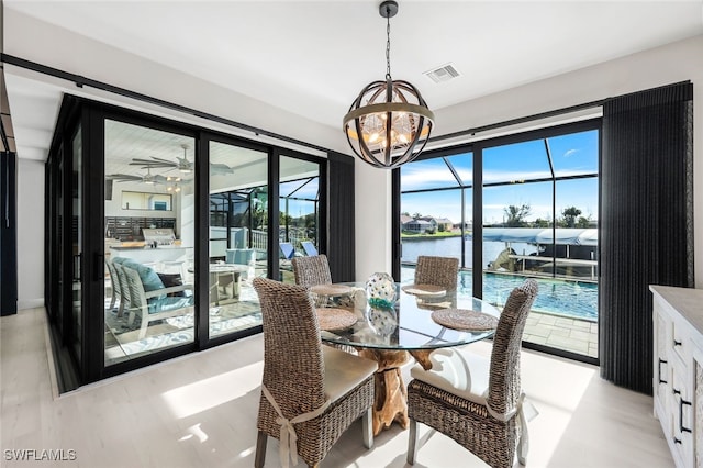 dining area with light wood-type flooring, plenty of natural light, ceiling fan with notable chandelier, and a water view