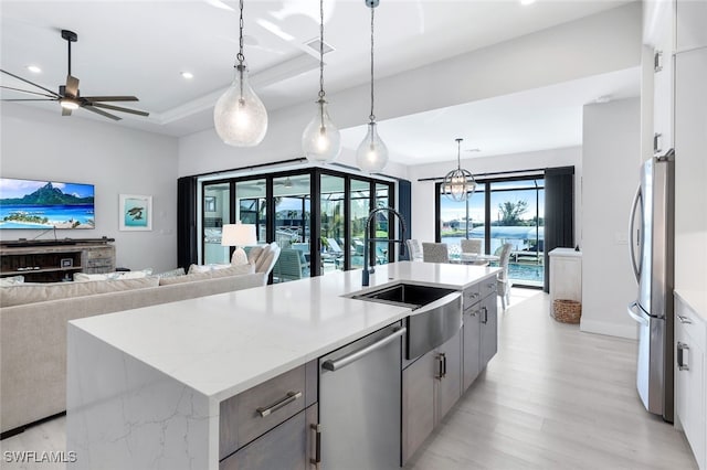 kitchen with ceiling fan with notable chandelier, decorative light fixtures, a center island with sink, stainless steel appliances, and light wood-type flooring