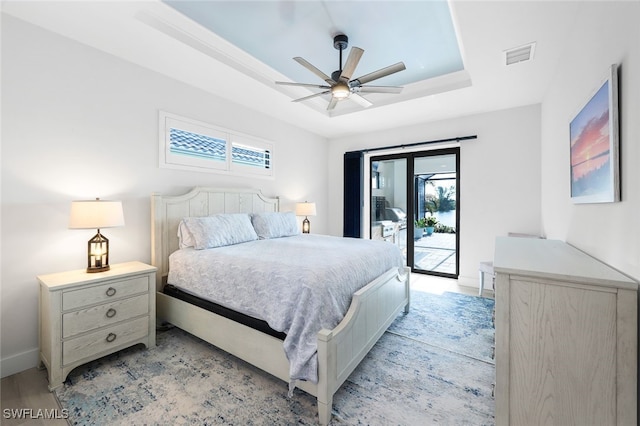 bedroom featuring access to exterior, a tray ceiling, ceiling fan, and multiple windows