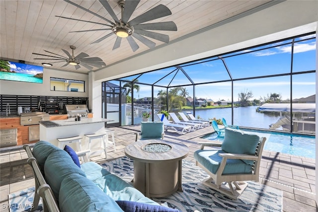 view of patio with a lanai, an outdoor living space with a fire pit, a water view, an outdoor kitchen, and ceiling fan