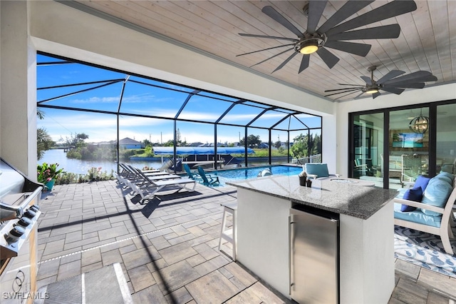 view of patio / terrace featuring a lanai, a water view, exterior kitchen, ceiling fan, and an outdoor bar