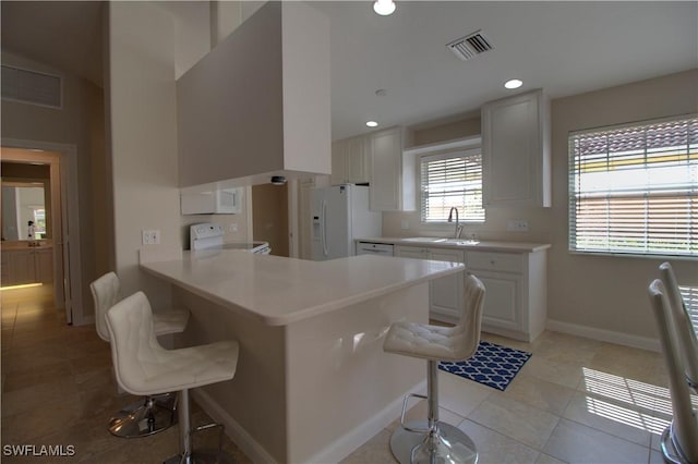 kitchen with white appliances, visible vents, a kitchen breakfast bar, light countertops, and a sink