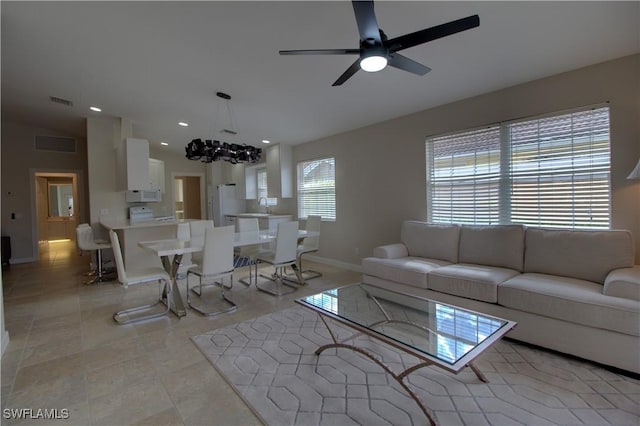 living room with light tile patterned floors, recessed lighting, visible vents, baseboards, and ceiling fan with notable chandelier