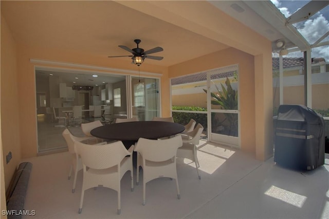 view of patio featuring glass enclosure, ceiling fan, outdoor dining area, and area for grilling