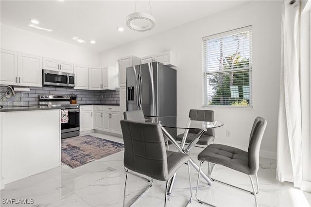 kitchen with backsplash, white cabinetry, stainless steel appliances, and hanging light fixtures