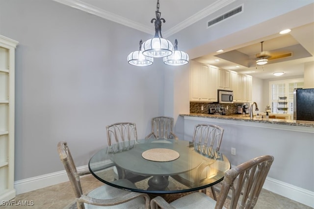 tiled dining room with a tray ceiling, crown molding, and ceiling fan with notable chandelier