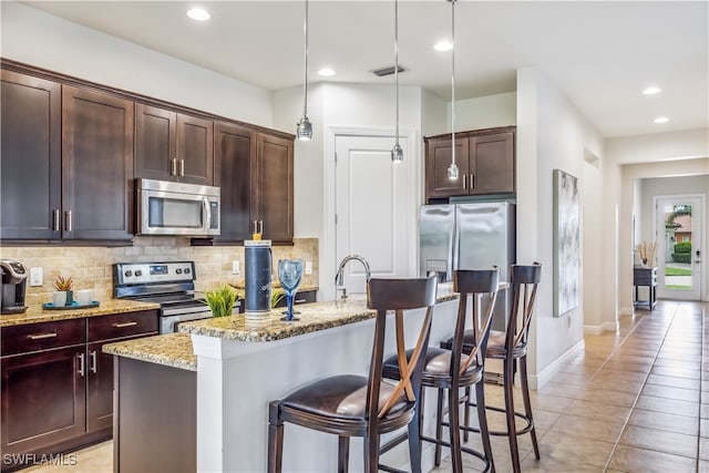 kitchen featuring backsplash, a kitchen island with sink, stainless steel appliances, light stone counters, and light tile patterned flooring