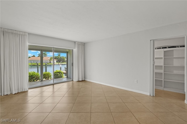 empty room with light tile patterned floors, a water view, and baseboards