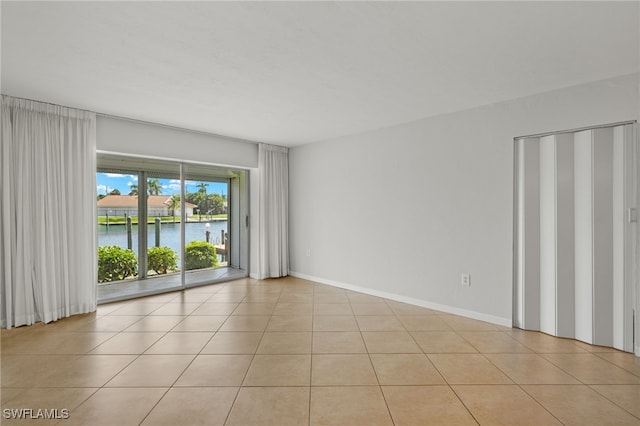 unfurnished room featuring a water view, light tile patterned floors, and baseboards