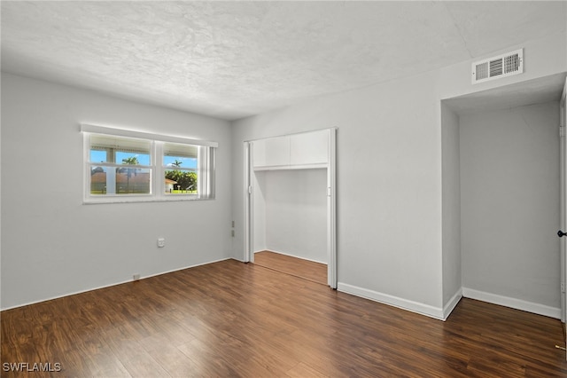 unfurnished bedroom featuring dark wood-type flooring, a closet, visible vents, and a textured ceiling