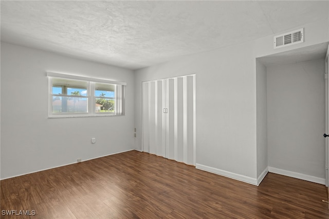 empty room with a textured ceiling, dark wood finished floors, visible vents, and baseboards