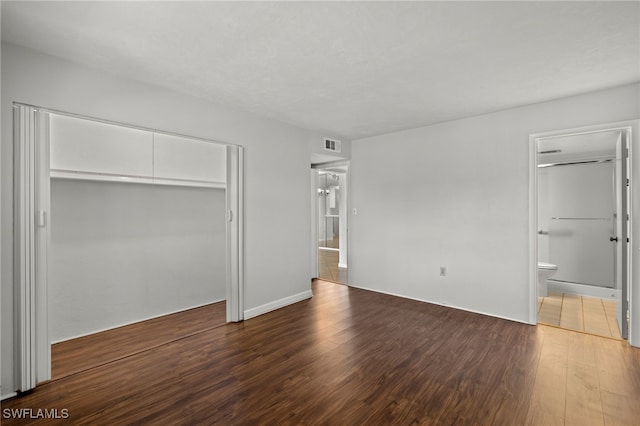 unfurnished bedroom featuring ensuite bath, visible vents, dark wood finished floors, and a closet