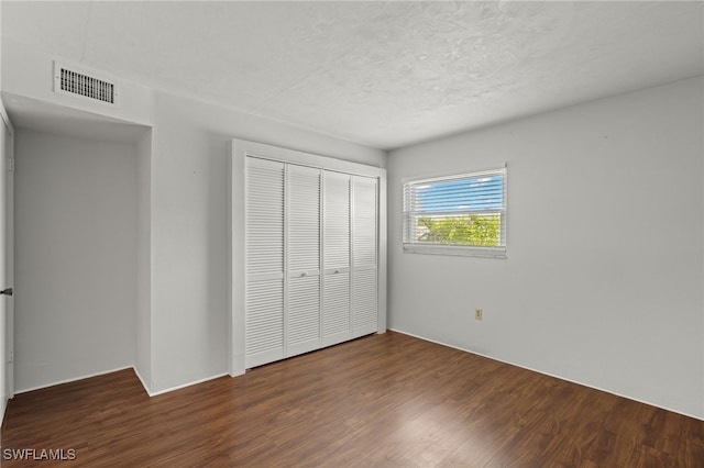 unfurnished bedroom with dark wood-style floors, a textured ceiling, visible vents, and a closet