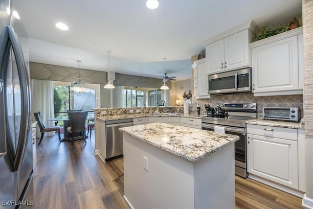 kitchen with a center island, hanging light fixtures, appliances with stainless steel finishes, white cabinetry, and kitchen peninsula