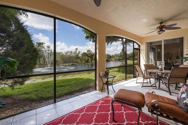 sunroom featuring ceiling fan and a water view