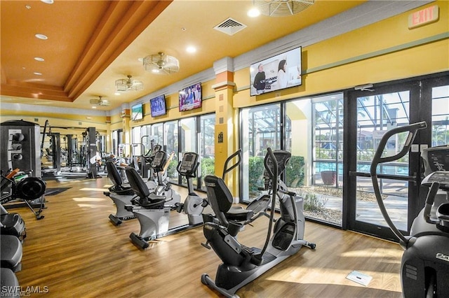 gym featuring light wood-style flooring, visible vents, and a tray ceiling