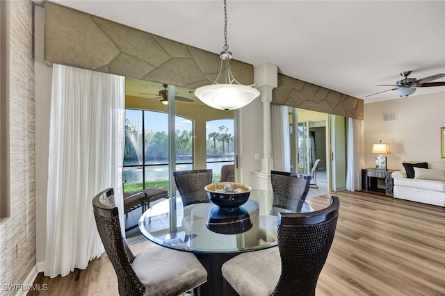 dining room with visible vents, a ceiling fan, wood finished floors, a water view, and ornate columns