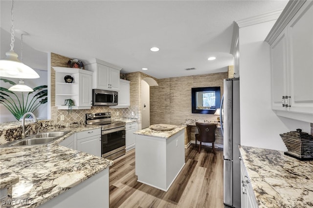 kitchen featuring a center island, decorative light fixtures, stainless steel appliances, white cabinetry, and a sink