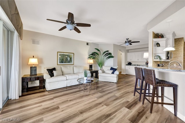 living room with ceiling fan, light wood-type flooring, visible vents, and baseboards