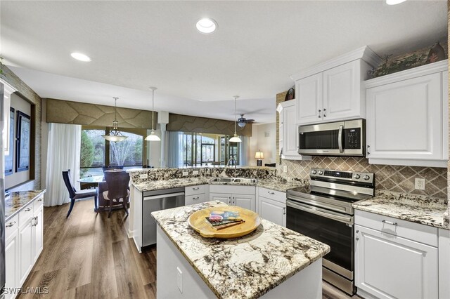 kitchen featuring pendant lighting, stainless steel appliances, a kitchen island, a sink, and a peninsula