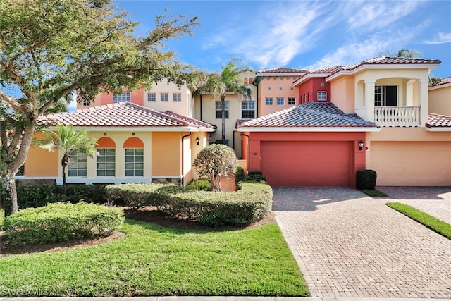 mediterranean / spanish home with decorative driveway, a tiled roof, a front lawn, and stucco siding