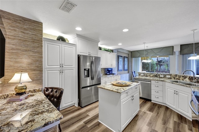 kitchen featuring stainless steel appliances, white cabinetry, hanging light fixtures, and a sink