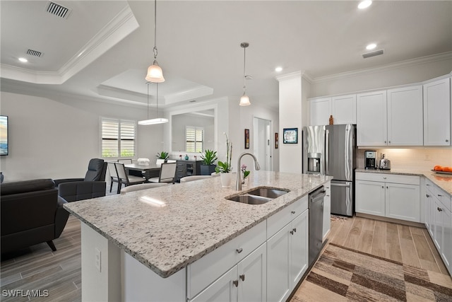 kitchen with light hardwood / wood-style floors, sink, a tray ceiling, and an island with sink