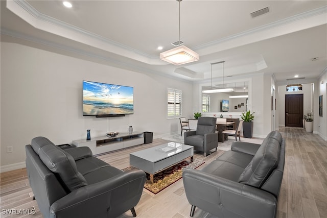 living room with a tray ceiling, ornamental molding, and light wood-type flooring