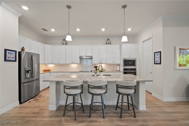 kitchen featuring decorative backsplash, light hardwood / wood-style flooring, white cabinets, a center island with sink, and stainless steel appliances