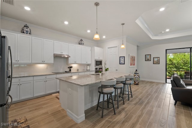 kitchen featuring light wood-type flooring, an island with sink, white cabinets, light stone countertops, and stainless steel appliances