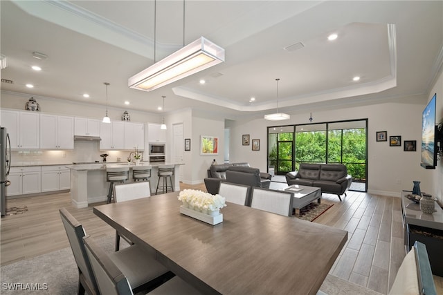 dining room featuring a raised ceiling, light hardwood / wood-style flooring, and crown molding