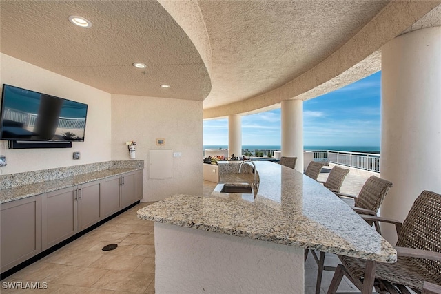 kitchen featuring a sink, gray cabinetry, light stone countertops, a kitchen breakfast bar, and a kitchen island with sink