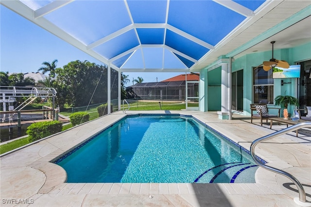 view of pool with glass enclosure, a patio area, and ceiling fan