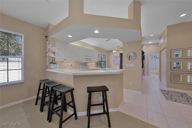 kitchen featuring range with electric stovetop, light tile patterned flooring, white cabinets, a kitchen bar, and kitchen peninsula